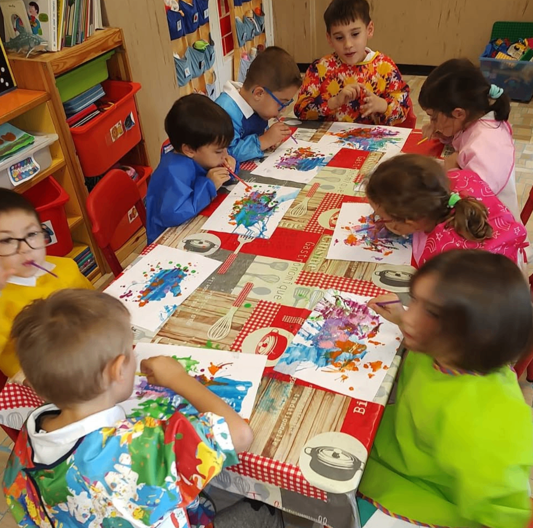 Bambini impegnati in un'attività pittorica insieme al tavolo